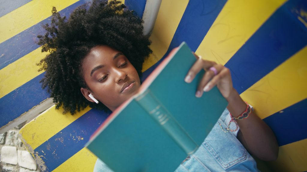 Closeup teen reading book aloud lying on bench outdoors. Girl enjoy literature